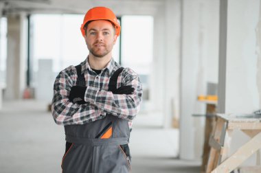 İnşaat alanında sabit şapka takan ve iş üniforması giyen kendine güvenen inşaat işçisi kameraya bakıyor.