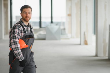 Bitmemiş bir binada yürürken miğfer taşıyan inşaat işçisi, projenin devam eden ilerlemesini gösteriyor.