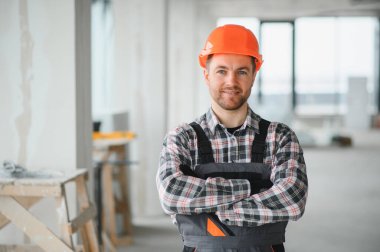 Turuncu bir kask takan kendine güvenen HVK teknisyeni inşaat alanında kollarını kavuşturup gülümsüyor.