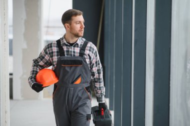 Hvac teknisyeni inşaat halindeki bir binaya giriyor. Elinde aletler ve kaskla havalandırma sistemini kontrol ediyor.