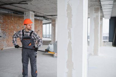 Boya silindiri kullanan profesyonel bir müteahhit, yenilenmekte olan bir binanın duvarlarına yeni bir kat boya sürüyor, iç mimari çalışmaların nasıl sonuçlandığını gösteriyor.