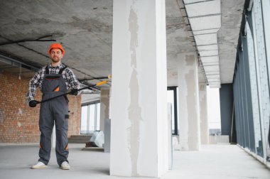 İnşaat işçisi uzun bir tekerlekli fırça tutuyor, inşaat sahasında bir kolon boyamaya hazırlanıyor.