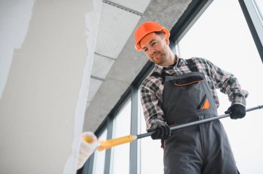 Profesyonel bir inşaatçı boya silindiri kullanıyor, inşaat sahasında duvarları yeniliyor, iç iyileştirmeler ve bakım üzerinde çalışıyor.