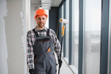 Profesyonel müteahhit koruyucu kask takıyor ve inşaat halindeyken boya silindiri tutuyor.
