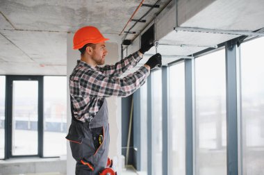 İnşaat işçisi inşaat halindeki bir binaya havalandırma sistemi kurmak için ingiliz anahtarı kullanıyor, hassasiyet ve güvenliğe odaklanıyor.