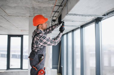 İnşaat halindeki bir binaya elektrikli matkap kullanarak havalandırma sistemi kuran yetenekli bir işçi.