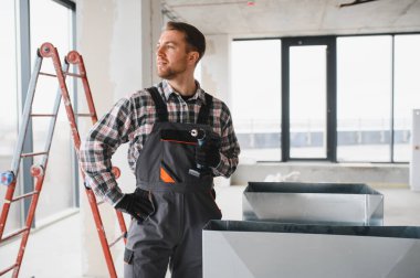 İnşaat işçisi kablosuz tornavida tutuyor, inşaat halindeki bir binaya havalandırma sistemi kuruyor.