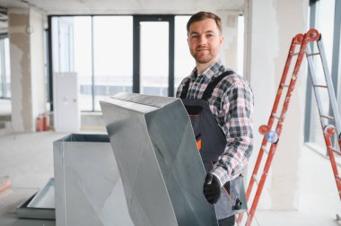 Hvac teknisyeni inşaat halindeki bir binada kurulum sırasında havalandırma sisteminin bir parçasını taşıyor