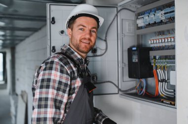 Güvenlik kaskı takan elektrikçi inşaat veya yenileme sırasında elektrik paneli üzerinde çalışıyor.