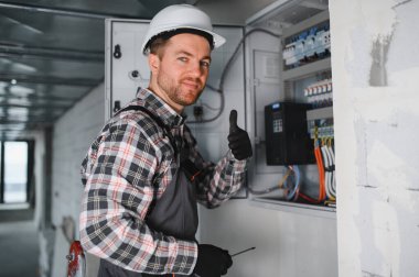 Güvenlik kaskı takan elektrikçi inşaat halindeki bir binanın elektrik panelinde çalışıyor.