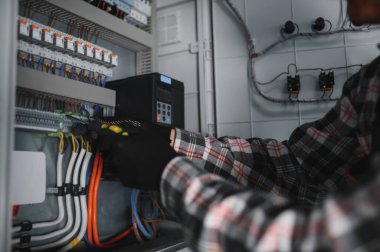 Güvenlik kaskı takan elektrikçi inşaat halindeki elektrik kontrol panelini kontrol ediyor.