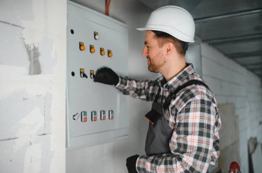 İnşaat veya yenileme sırasında koruyucu kask takan elektrikçi ve eldiven işletim kontrol paneli