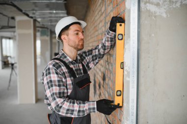 İnşaatçı tuğla duvarın yüksekliğini ruh seviyesini kullanarak kontrol ediyor, bina inşaatı sırasında hassas bir hizalama sağlıyor