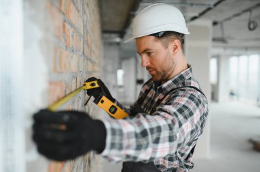 Tadilat sırasında koruyucu kask ve eldiven giyen inşaatçı mezura ve ruhsal seviye kullanıyor.