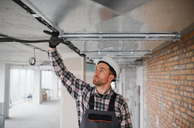 Güvenlik kaskı takan inşaat işçisi inşaat halindeki bir binaya havalandırma sistemi kuruyor.