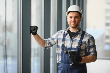 Modern bir binaya kablosuz tornavida ve sabit şapka takan inşaat işçisi.