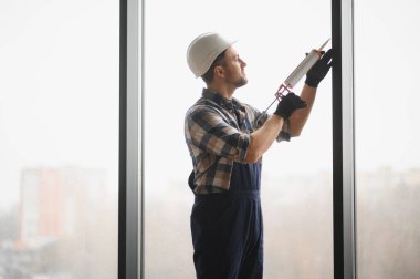 Yeni inşa edilen bir binada pencere kurulumu sırasında dolgu macunu uygulayan yapıcı, en iyi performans için kalite ve kesinlik sağlar