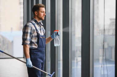 Bir ofis binasındaki büyük bir pencereye cam spreyi sıkarak, cam sileceği ile temizlemeye hazırlanıyor.
