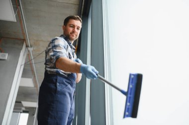 Modern ofis binasında cam silici, cam silici ve mavi eldiven kullanıyor.