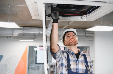 Elektrikçi güvenlik kaskı ve eldiven takarak havalandırma sistemi üzerinde çalışıyor.