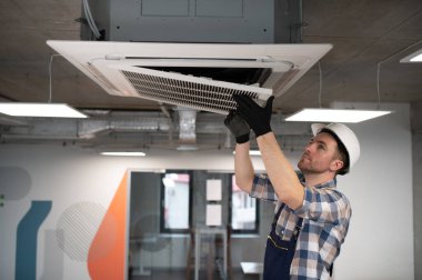 Hvac teknisyeni, kasketli ve eldivenli. Modern bir ofis binasına klima sistemi kuruyor.