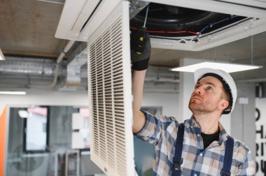 Hvac teknisyeni güvenlik kaskı takıyor ve tornavida kullanıyor, tavanda havalandırma ünitesini tamir ediyor.