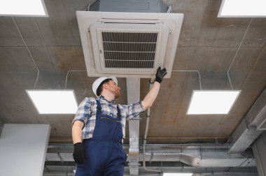 Hvac teknisyeni inşaat halindeki binanın tavanında yeni kurulmuş klima ünitesini inceliyor.
