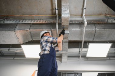 Hvac teknisyeni güvenlik kaskı takıyor ve bir inşaat sahasına havalandırma sistemi kuruyor.