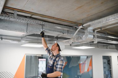 Hvac teknisyeni yeni bir ofiste havalandırma ve havalandırma boruları üzerine çalışıyor.