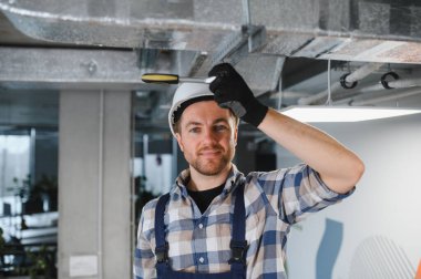 Modern ofis binasında havalandırma sistemi üzerinde çalışırken güvenlik kaskı takan ve ingiliz anahtarı kullanan Hvac teknisyeni