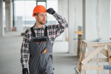İnşaat işçisi miğferini düzeltirken inşaat alanını yakından inceleyerek yenileme sürecinde güvenlik ve kalite sağlıyor.