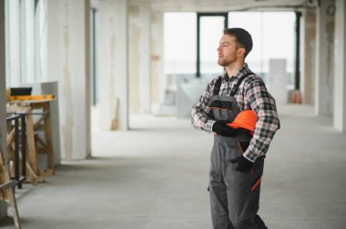 İnşaat işçisi, tadilat sırasında yürürken miğferini tutuyor ve bir inşaat alanını inceliyor.