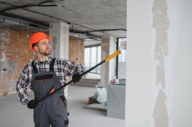 Boya silindiri kullanan profesyonel bir müteahhit, yenilenmekte olan bir binanın duvarlarına yeni bir kat boya sürüyor, iç mimari çalışmaların nasıl sonuçlandığını gösteriyor.