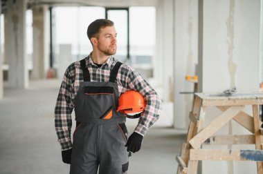 Üniformalı inşaat işçisi güvenlik kaskı tutuyor ve tadilat veya inşaat sürecinde inşaat alanını inceliyor.