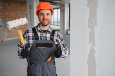 Üniforma giyen, elinde boya silindiri tutan ve tadilat sırasında el hareketi yapan bir mimar.
