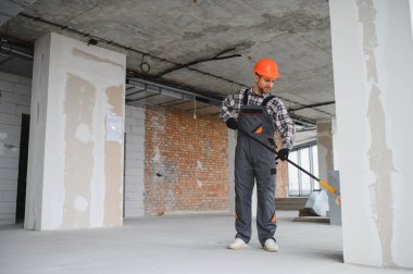 İnşaat işçisi koruyucu kask ve tulum giyiyor, uzun bir silindir kullanarak duvarı boyuyor, tadilat sırasında...