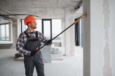 Boya silindiri kullanan profesyonel bir müteahhit, yenilenmekte olan bir binanın duvarlarına yeni bir kat boya sürüyor, iç mimari çalışmaların nasıl sonuçlandığını gösteriyor.