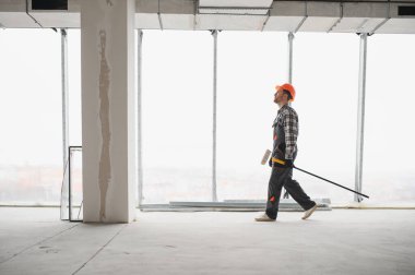 İnşaat işçisi inşaat alanında araç gereç, inşaat geliştirme, yenileme ve iyileştirme konsepti taşıyarak yürüyor