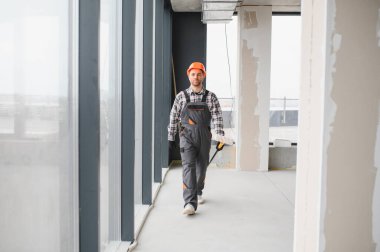 İnşaat işçisi inşaat halindeki bir binadan geçiyor. Alet taşıyor ve güvenlik ekipmanı takıyor.