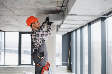 Güvenlik miğferi olan bir inşaatçı inşaat halindeki bir binaya havalandırma sistemi kuruyor.