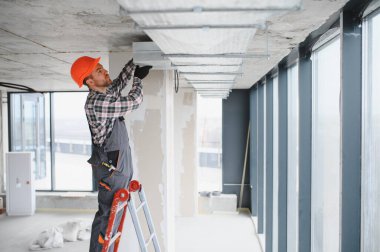 İnşaat işçisi inşaat halindeki bir binaya havalandırma ve havalandırma sistemi kuruyor.