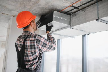 Güvenlik kaskı takan inşaatçı, inşaat halindeki bir binada havalandırma ve havalandırma sistemi kurulumunda çalışıyor.