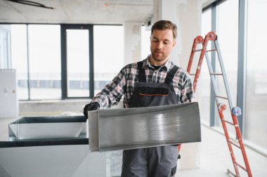 Hvac teknisyeni, havalandırma kanalını dikkatlice tutuyor ve inşaat halindeki bir binaya yerleştirmeye hazırlanıyor.