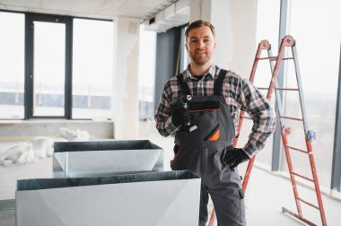 Hvac teknisyeni elinde matkap tutuyor, inşaat halindeki bir binaya havalandırma sistemi kuruyor.