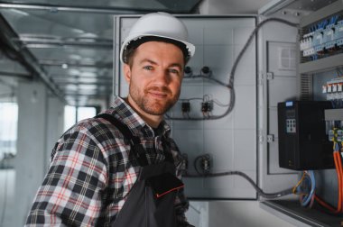 Güvenlik kaskı takan elektrikçi inşaat halindeki bir binanın elektrik panelinde çalışıyor.