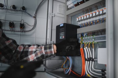 Güvenlik kaskı takan elektrikçi inşaat halindeki elektrik kontrol panelini kontrol ediyor.