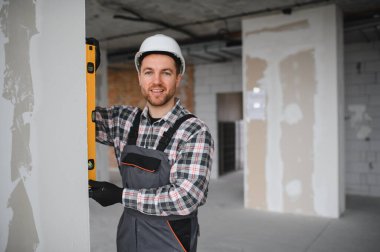 Ev yenileme sırasında ruh seviyesini kullanarak üniforma ve başlık takan inşaatçı duvarın dikey hizasını kontrol ediyor