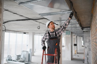 Bir inşaat alanında havalandırma ve havalandırma boruları üzerine çalışan erkek teknisyen.