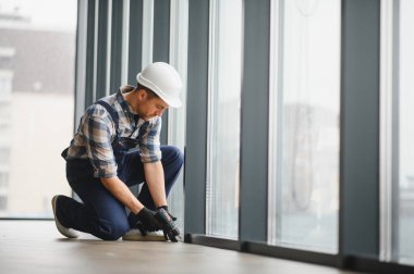 Elektrikli matkap kullanan usta işçiler, inşaat halindeki modern bir binaya pencere döşemek, hassas ve güvenli bir yer temin etmek,