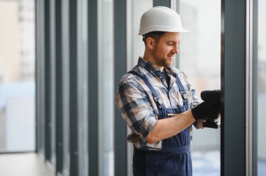 Modern bir binaya pencereler yerleştirilirken güvenlik kaskı takan ve kablosuz tornavida kullanan inşaat işçisi